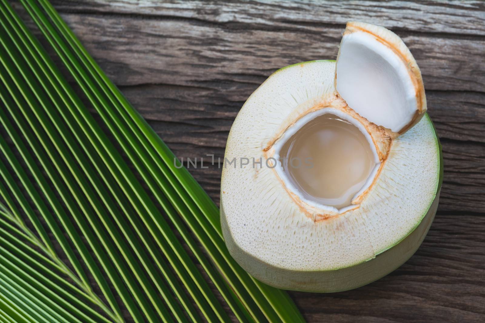 Fresh organic coconut water with coconut leaves on wooden table.