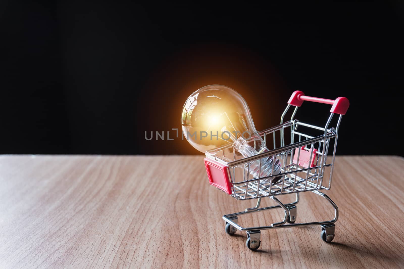 Energy saving light bulb with stacks of coins and shopping cart for saving, financial and shopping concept.