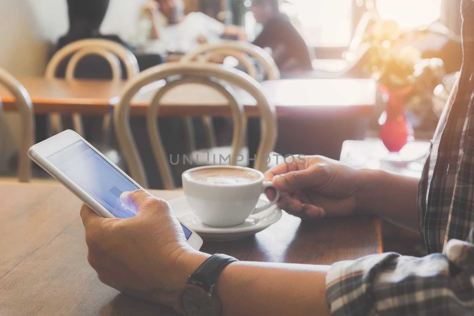 Male using a smart phone with coffee cup on wooden table.