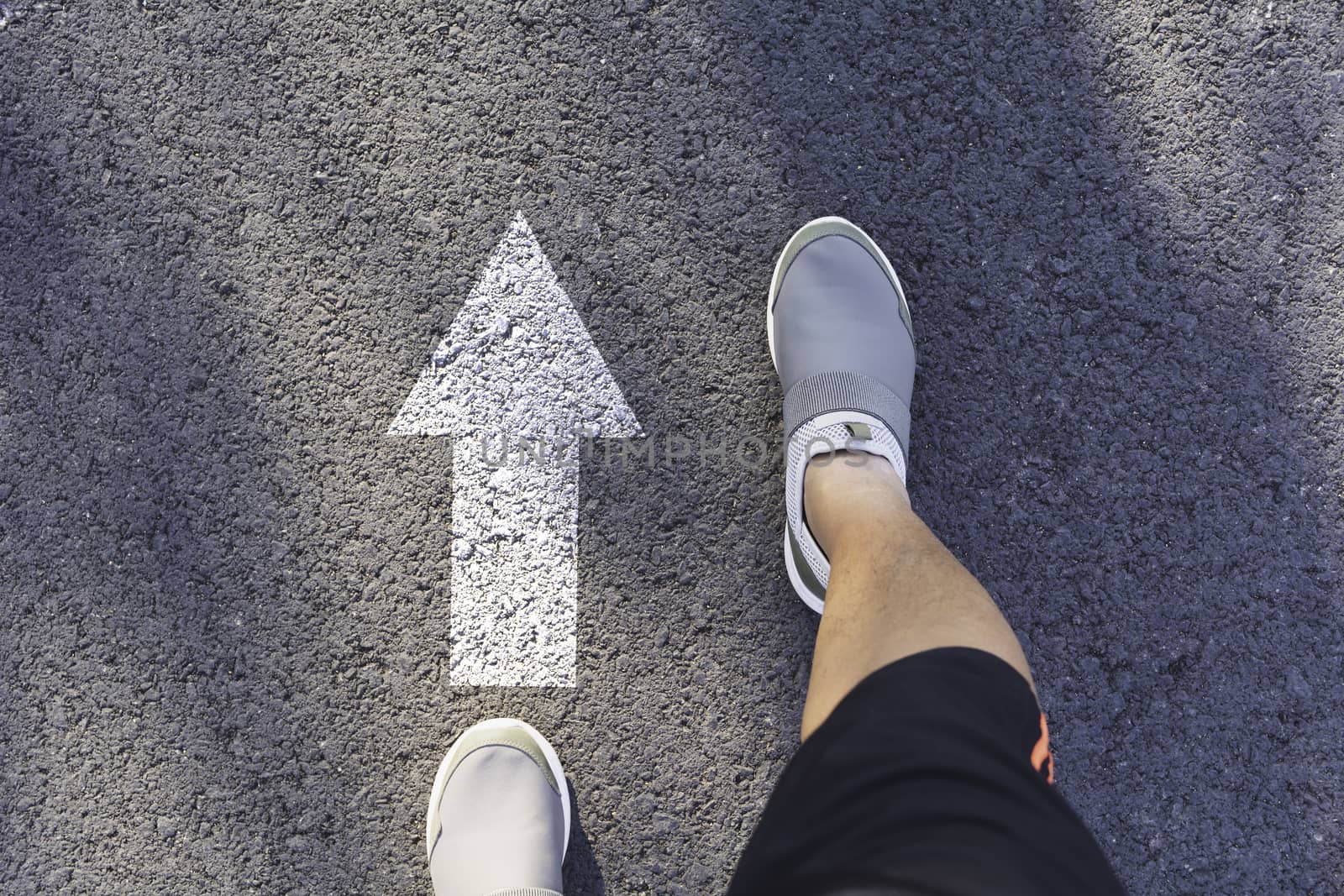Top view of man wearing white shoes choosing a way marked with white arrows. Chooses the right path concept.