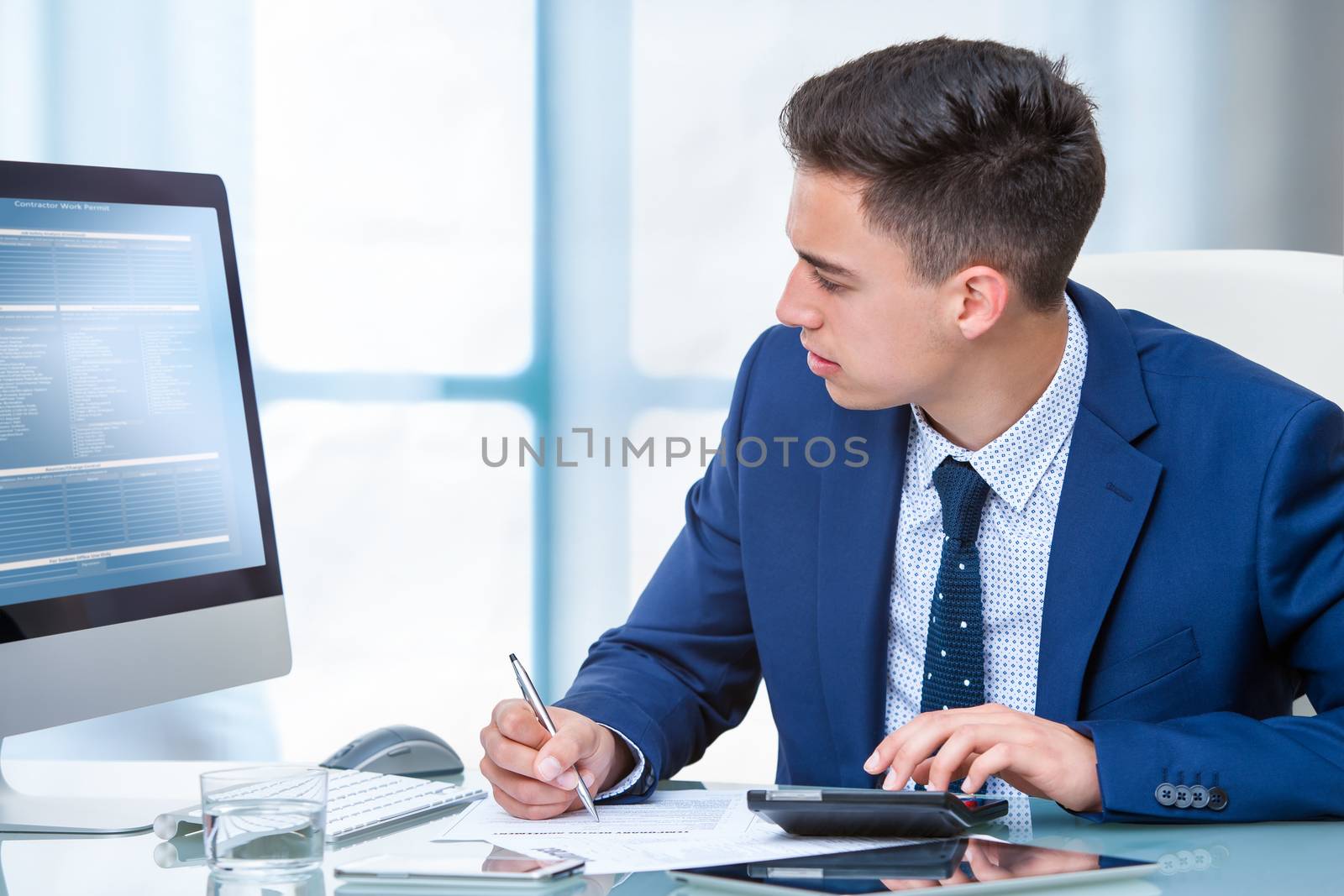 Close up portrait of young accountant doing on line internet transaction. Young man comparing documents on computer screen.