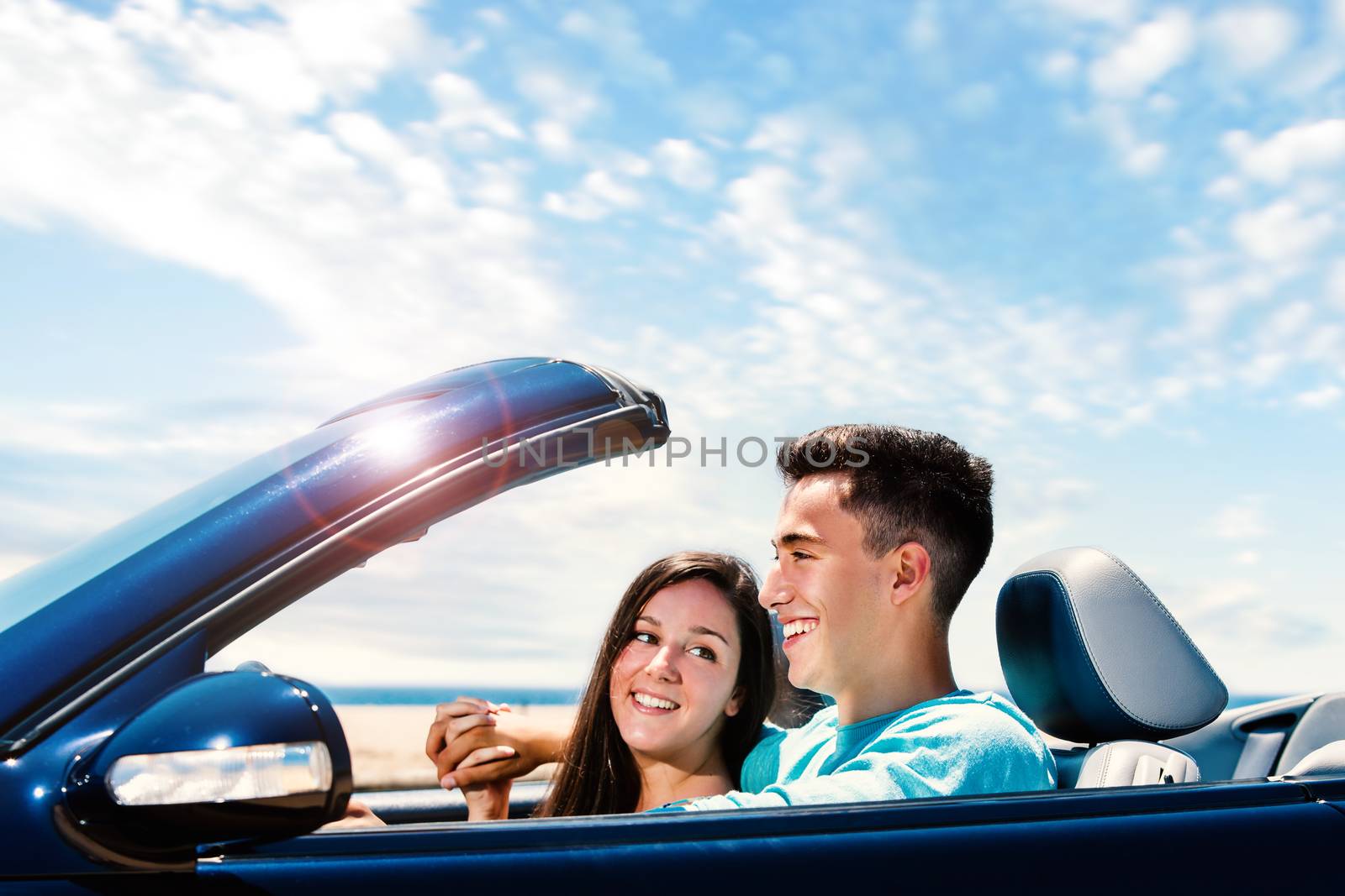 Close up portrait of Happy young couple driving blue convertible along seaside.