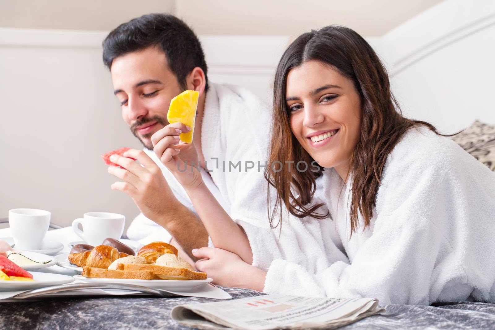 Close up portrait of couple having breakfast together on bed in hotel room.Couple wearing bathrobes.