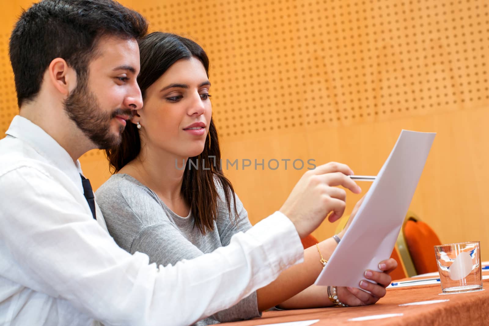 Portrait of young business couple reviewing documents in conference hall.Young man holding document and sharing information with woman.