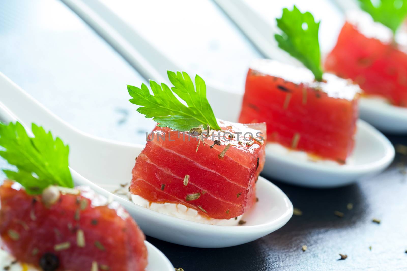 Macro close up of appetizing tuna morsel on ceramic spoons. Row of multiple tuna starters.