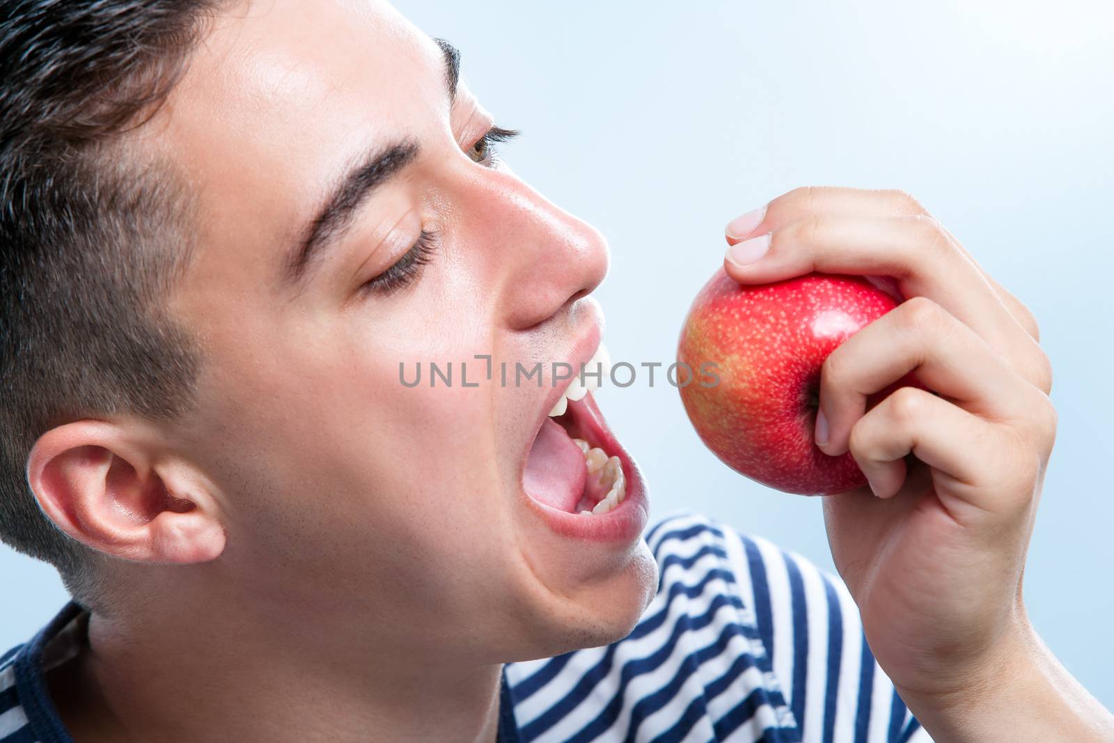 Extreme close up of male teenager about to bite a red apple.