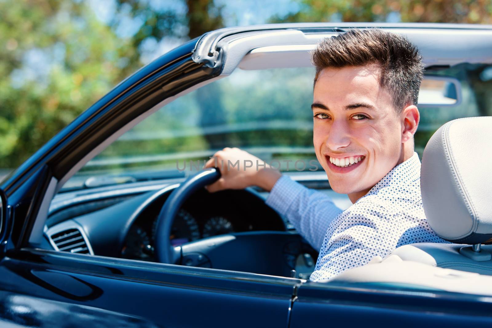 Portrait of attractive teen sitting in car. Young man sitting in convertible in driver seat.