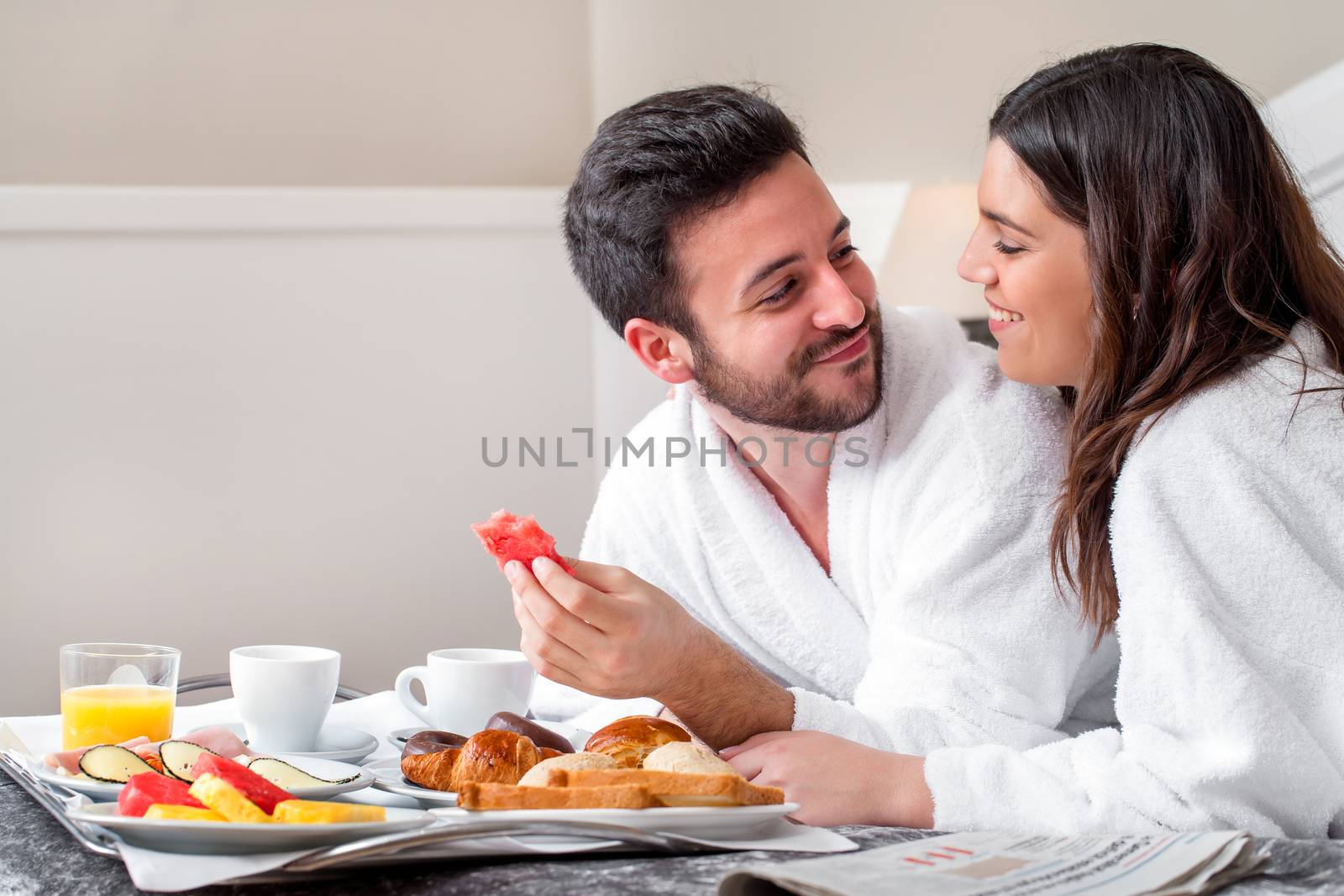 Close up portrait of young attractive couple enjoying breakfast in hotel room.