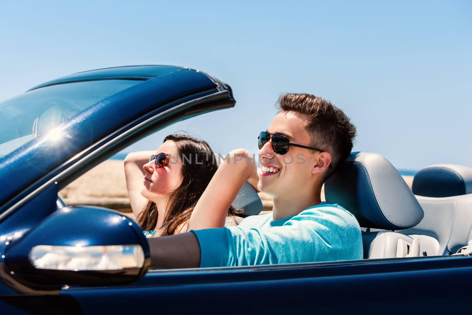 Portrait of attractive young man driving with girlfriend in blue cabriolet.