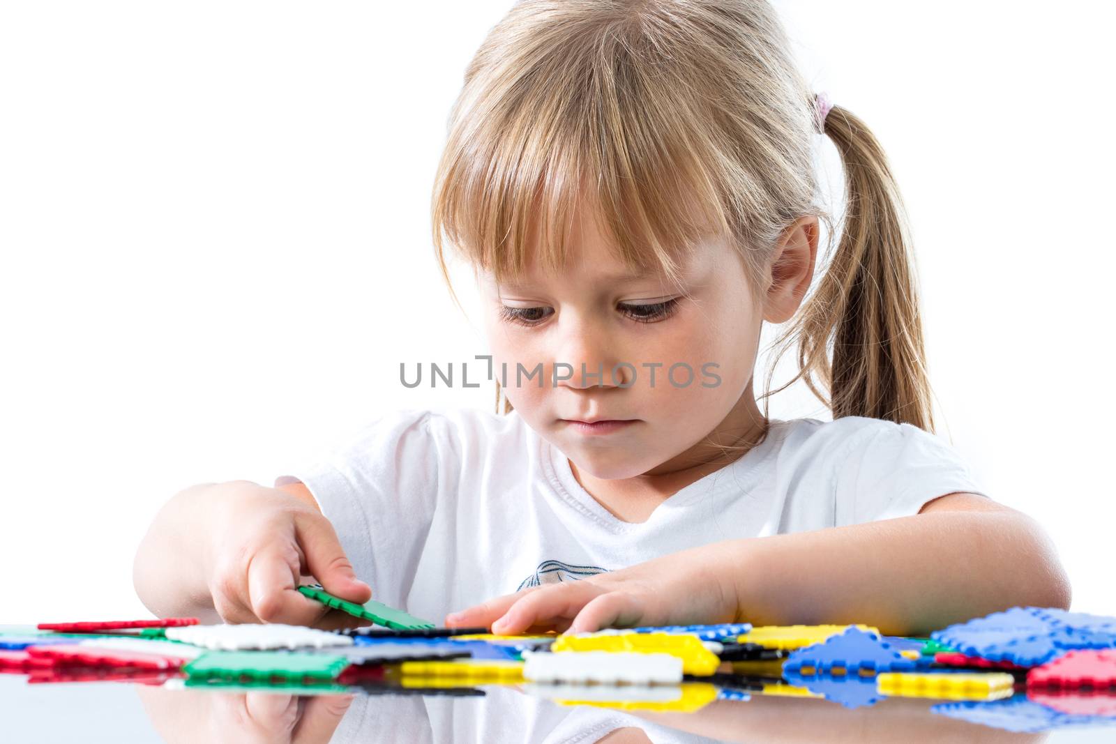 Close up portrait of cute little girl playing with puzzle pieces at table.Isolated on white background.