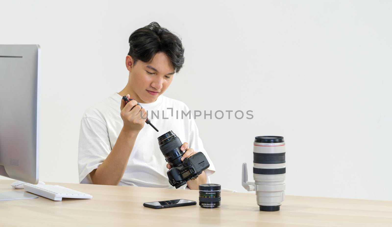 An Asian photographer is cleaning the camera and lens with a blower camera for cleaning on his desk. The atmosphere in the photo studio.