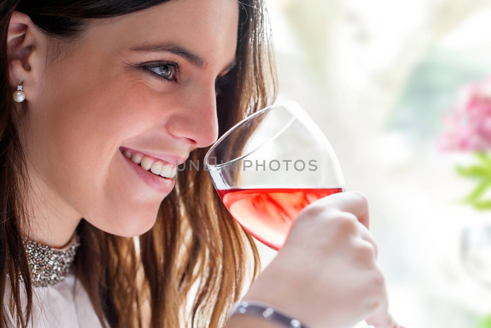 Close up face shot of attractive brunette with charming smile enjoying glass of wine.