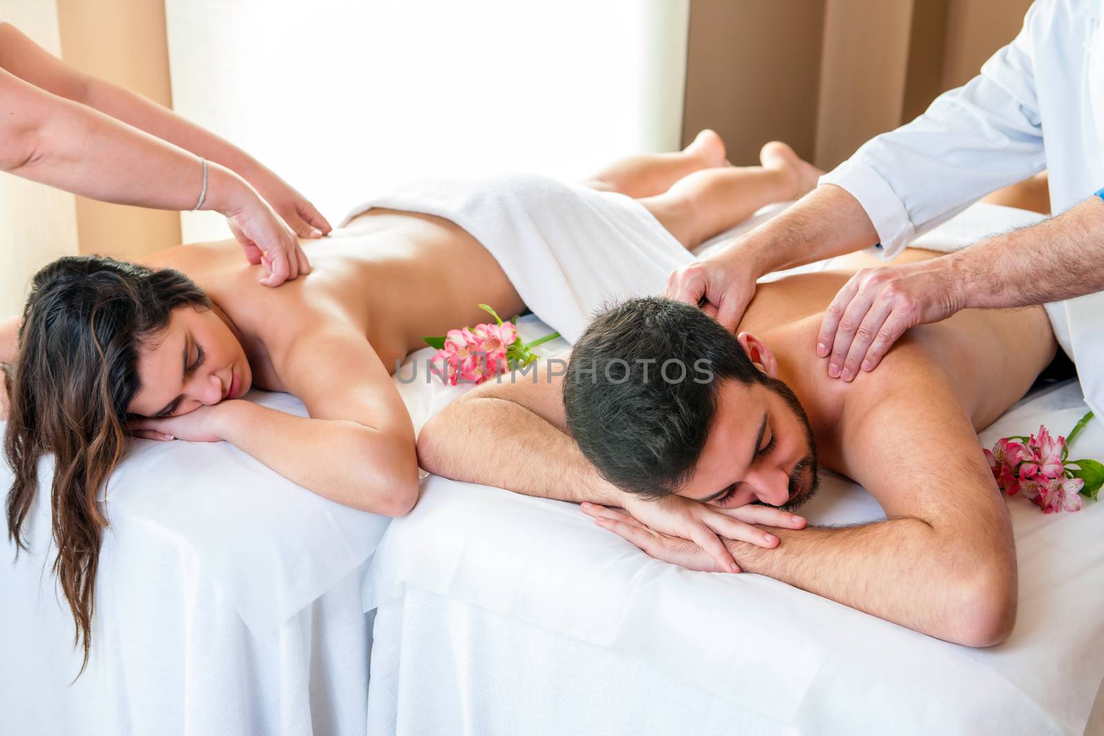 Close up of young couple enjoying simultaneous body massage in spa. Two therapists doing back massage on couple at the same time.