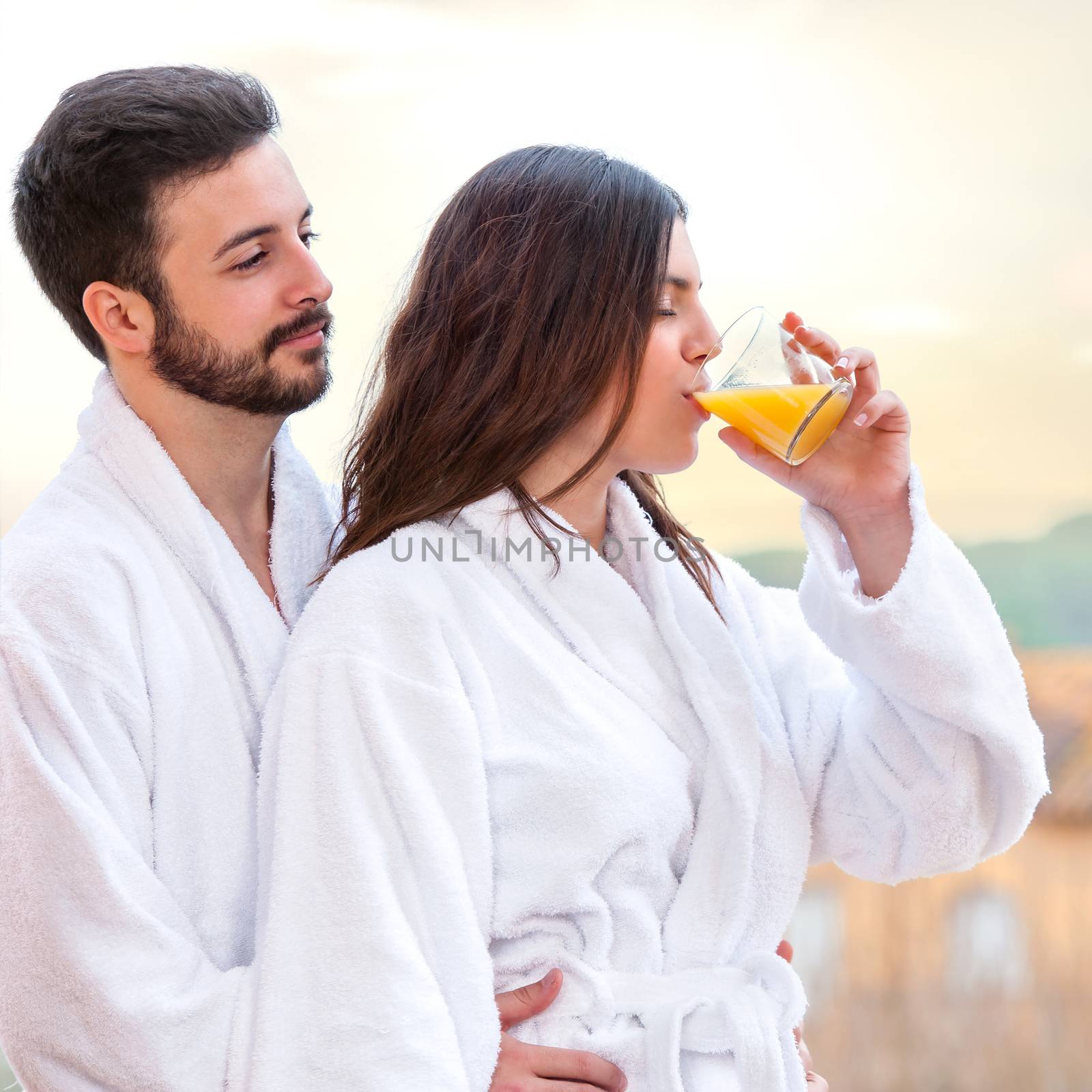 Close up of young couple in bathrobe. Woman drinking fruit juice.