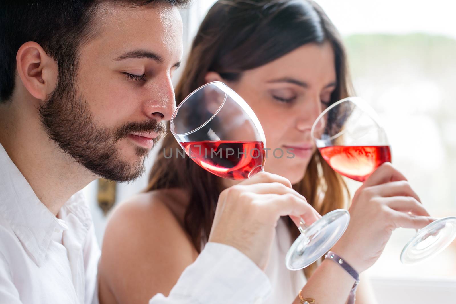 Close up portrait of young couple at wine tasting. Man and woman smelling wine with eyes closed.