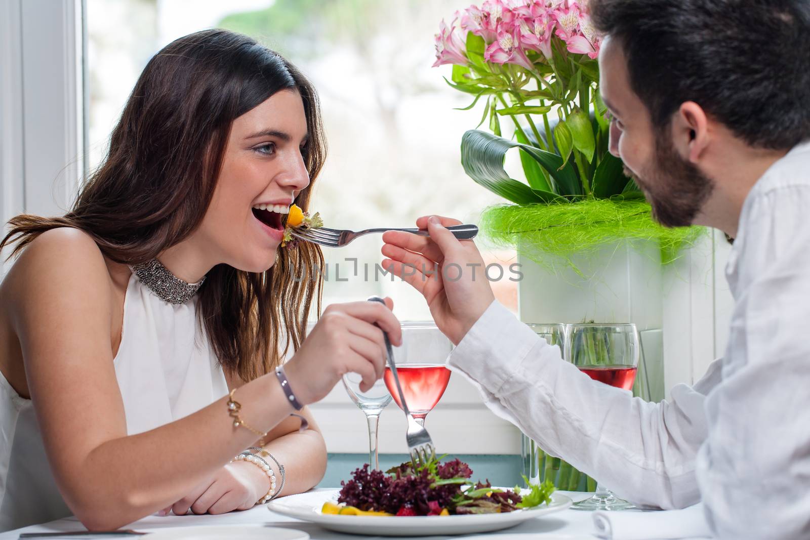 Close up portrait of young elegant couple having fun at dinner table in restaurant.Boy feeds girl with fork.