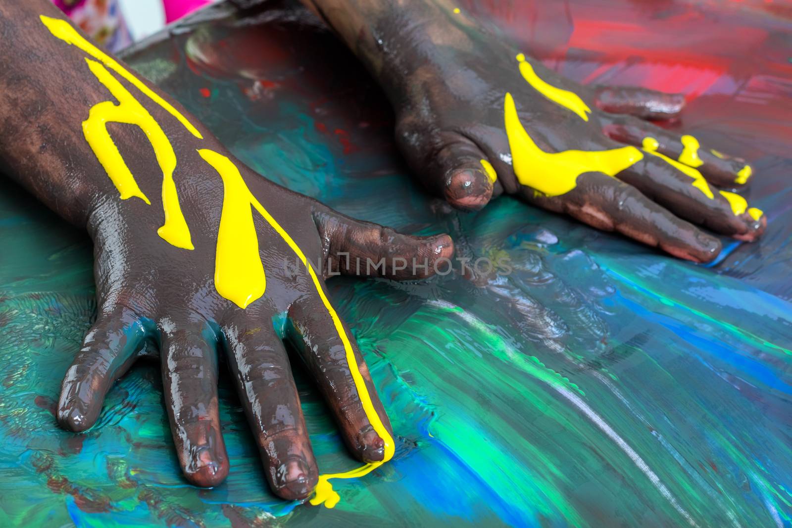 Close up of child’s hands painting at table.Colorful mosaic with paint covered hands.
