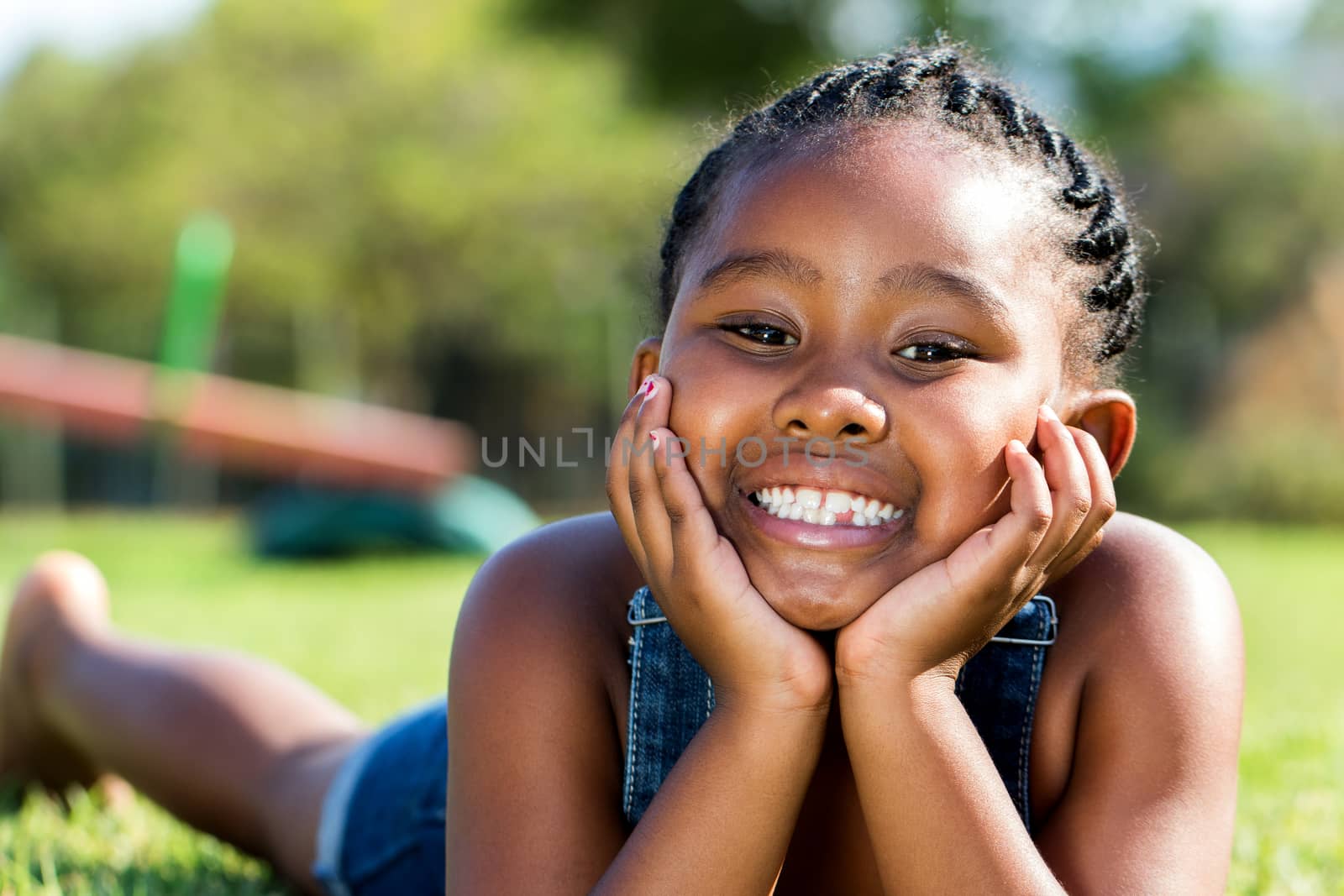 African girl laying with face on hands in park. by karelnoppe