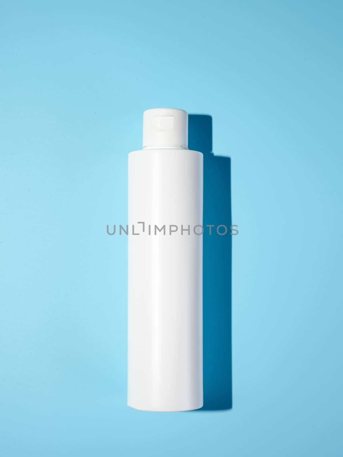 Empty white plastic bottle mockup in hard light. Top view or flat lay. Blank opaque bottle without packaging on blue background. Mock up for package design