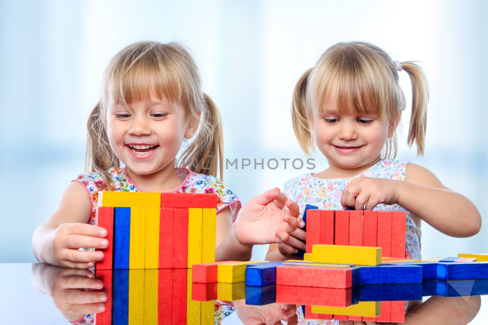 Close up portrait of two little girls playing with colorful wooden pieces at table.
