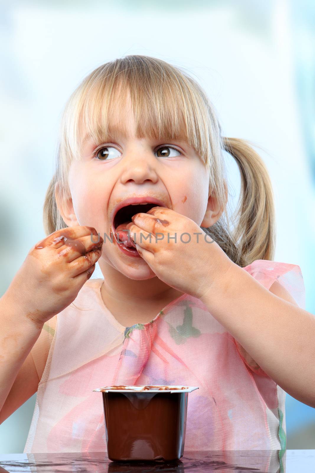 Close up portrait of cute infant eating chocolate yogurt with hands.Girl showing dirty face full of chocolate.