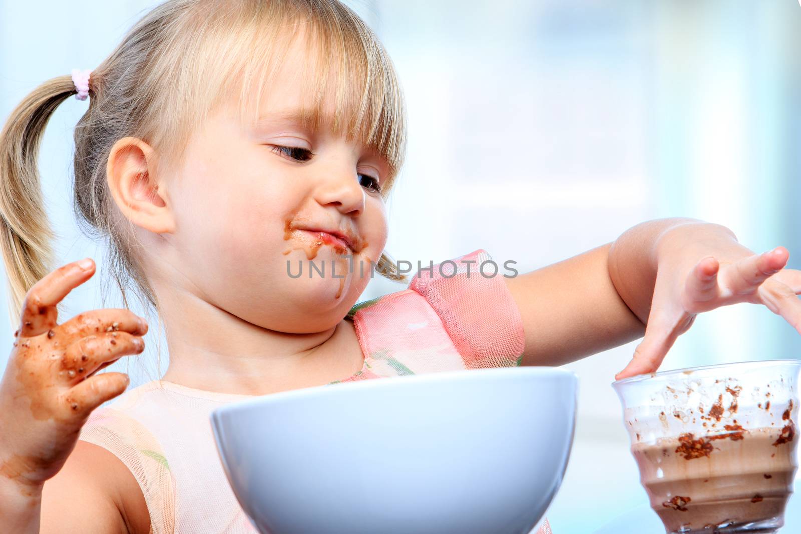Close up portrait of little girl at breakfast. Infant spilling and playing around with chocolate  milk.