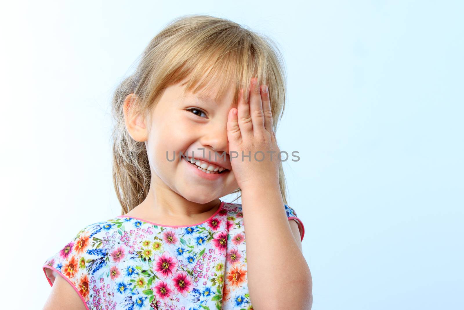 Close up portrait of Cute little girl closing one eye with hand against blue background.