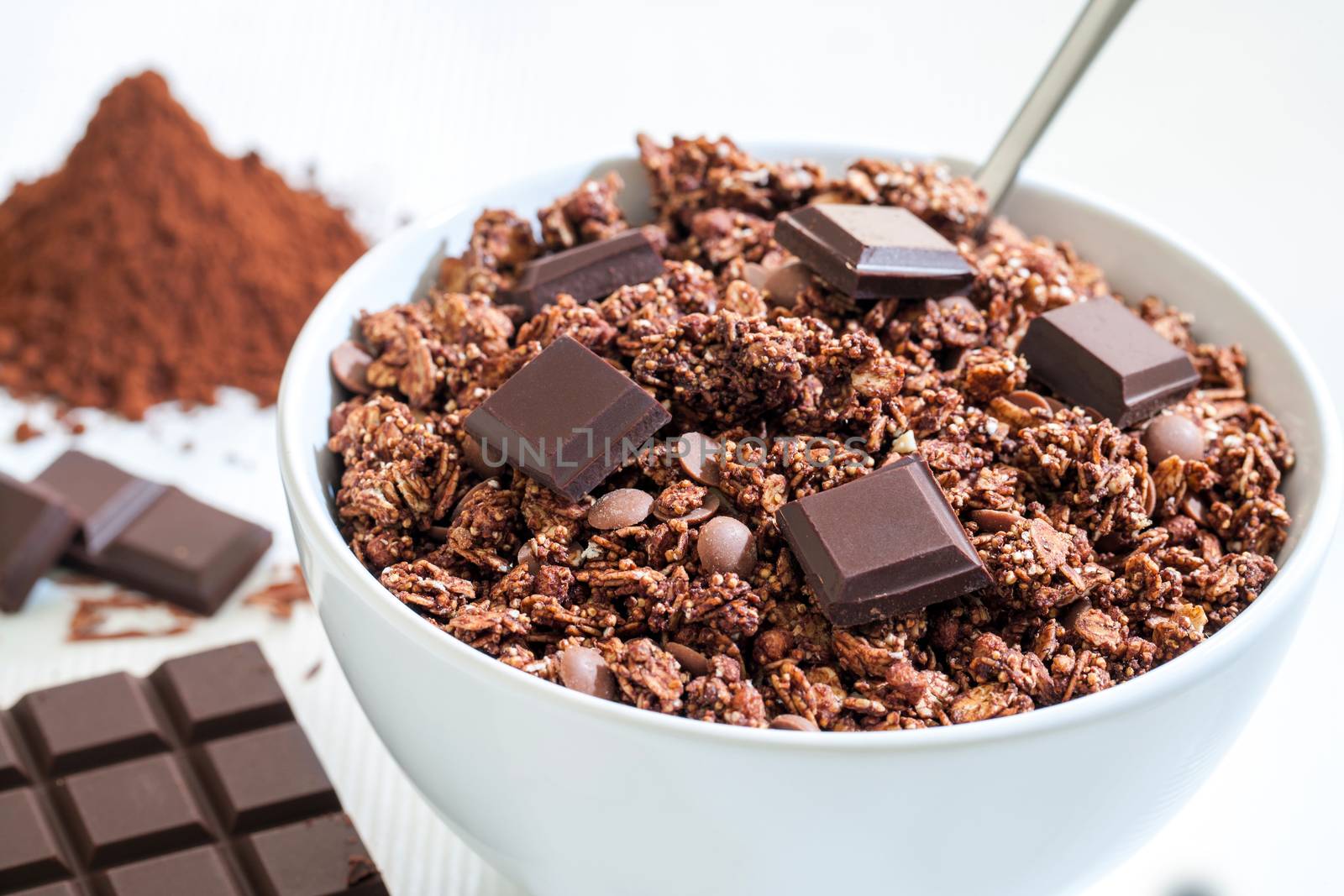 Extreme close up of white bowl with Chocolate Muesli.Chocolate slab and cacao powder in background.