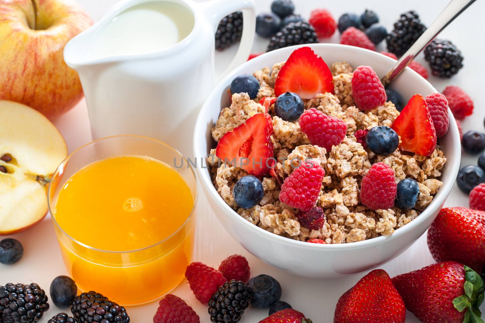 Macro close up of appetizing crunchy muesli bowl with red fruit. Fruits and fresh orange juice next to bowl.