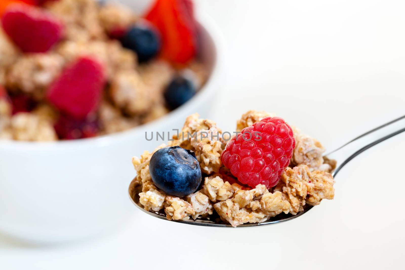 Extreme close up of spoon with crunchy red fruit muesli and bowl in background.