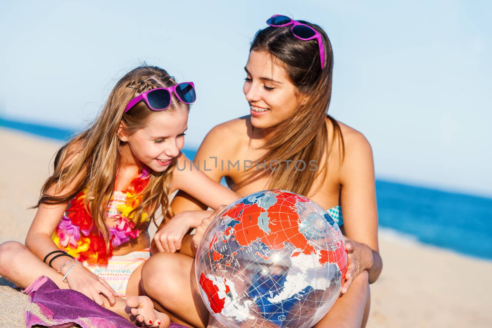 Close up conceptual image of Young girls sitting on beach discussing next holiday destination.Mother showing daughter world map on inflatable beach ball.