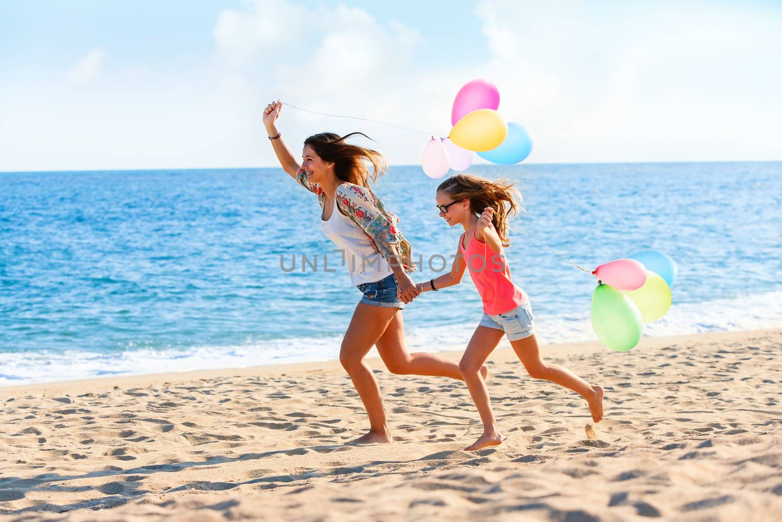 Action portrait of Young girls running with colorful balloons on beach.
