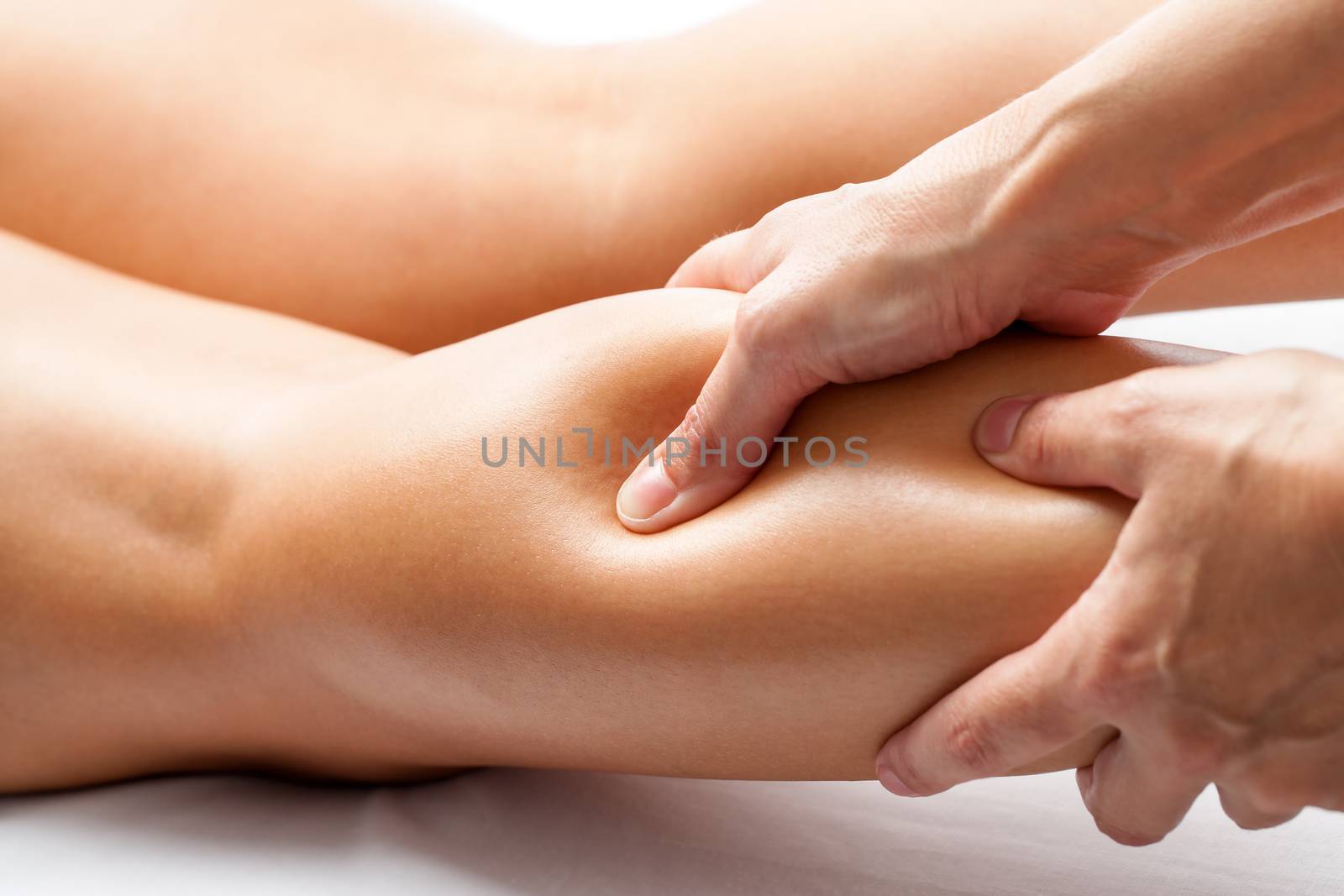 Extreme close up of osteopath applying pressure with thumb on female calf muscle.