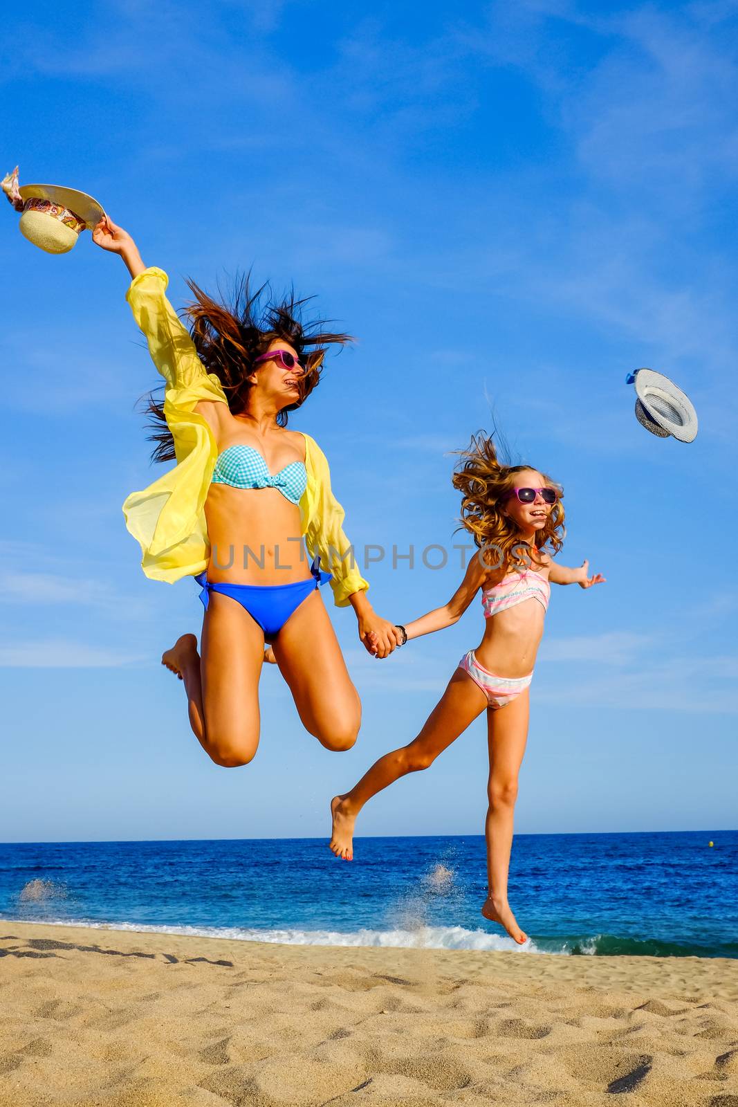 Young girls in swimwear jumping on beach. by karelnoppe