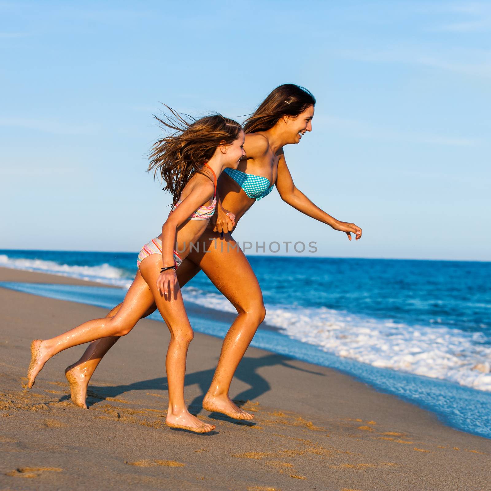 Action portrait of Young Mother running with daughter on beach.Two young girls in swimwear running to water.