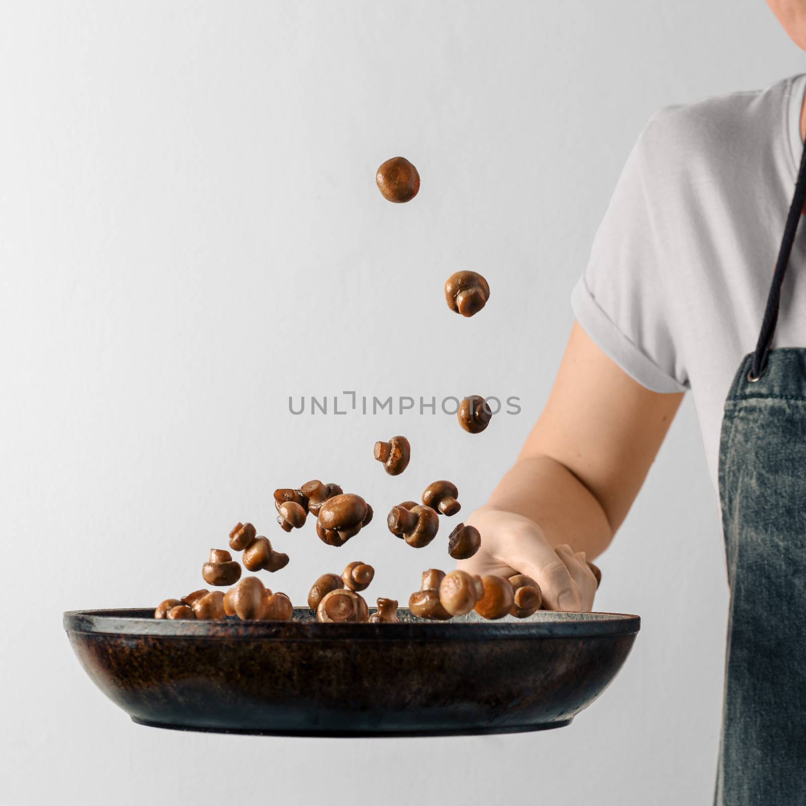 Chef woman preparing mini champignons in skillet frying them. Flying ingredients over pan with copy space. Hotel and caternig business, menu in restaurants, book of recipes concept. White background