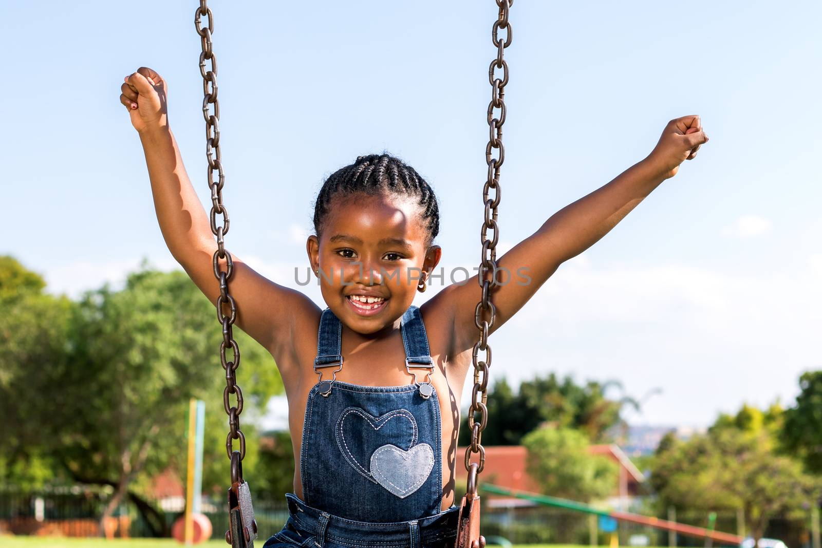 Close up portrait of Happy African kid raising arms on swing in park.