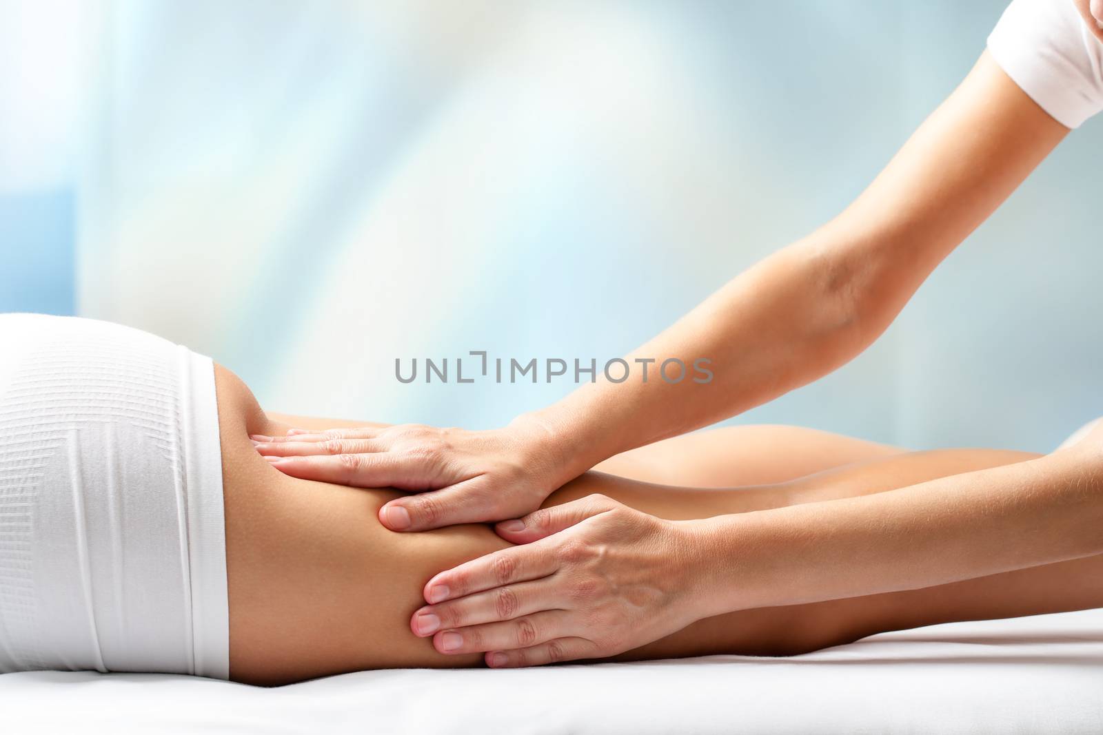 Therapist massaging upper back part of female leg. Hands applying pressure on hamstrings.