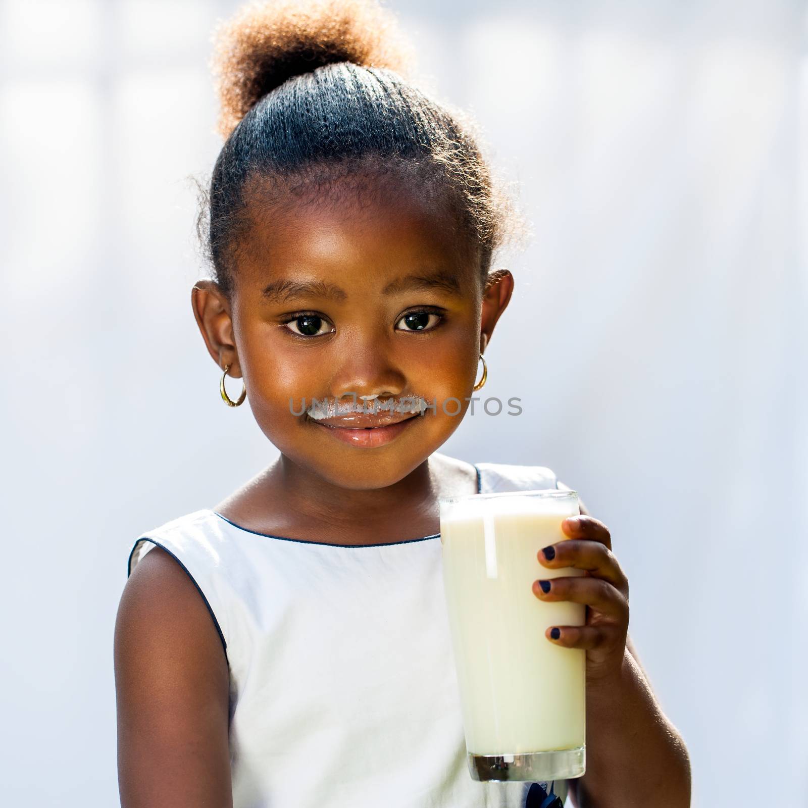 Close up portrait of adorable little African girl drinking glass of milk.Isolated against light background.
