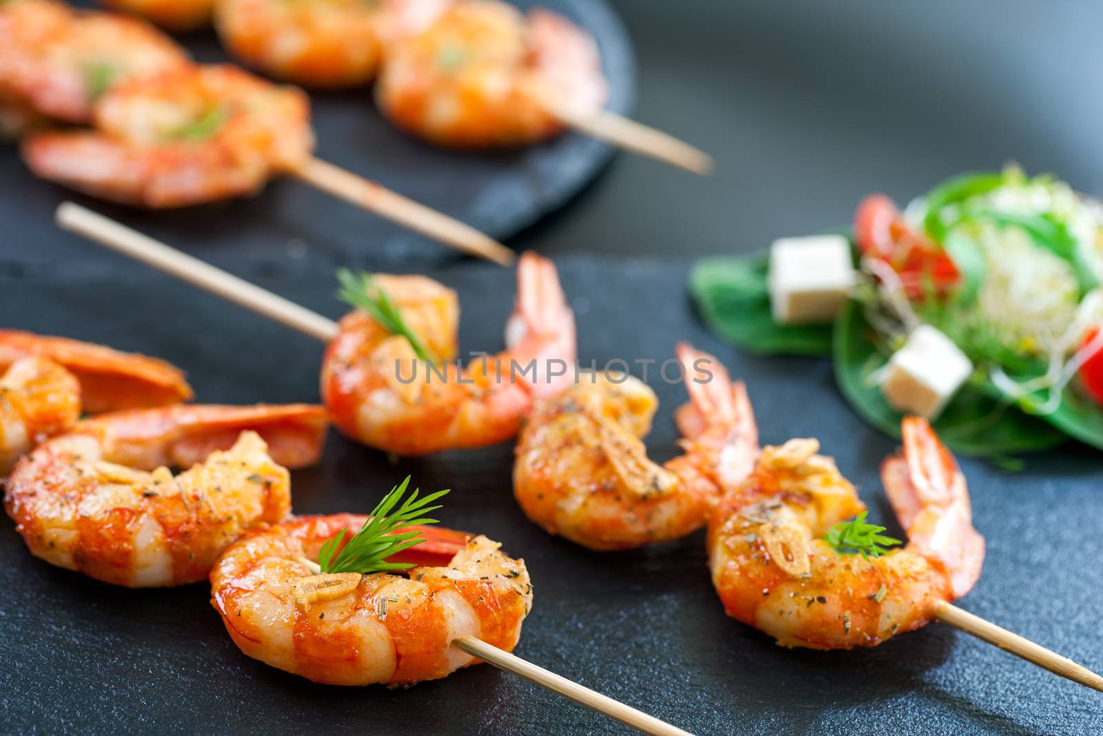 Macro close up of catering shrimp brochettes grilled with herbs. Out of focus salad in background.