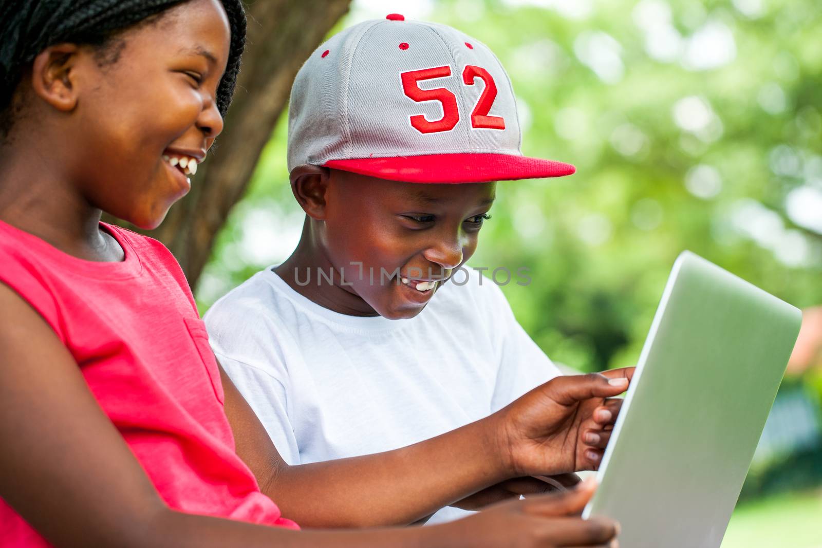 Close up portrait of African youngsters enjoying time with laptop in park.