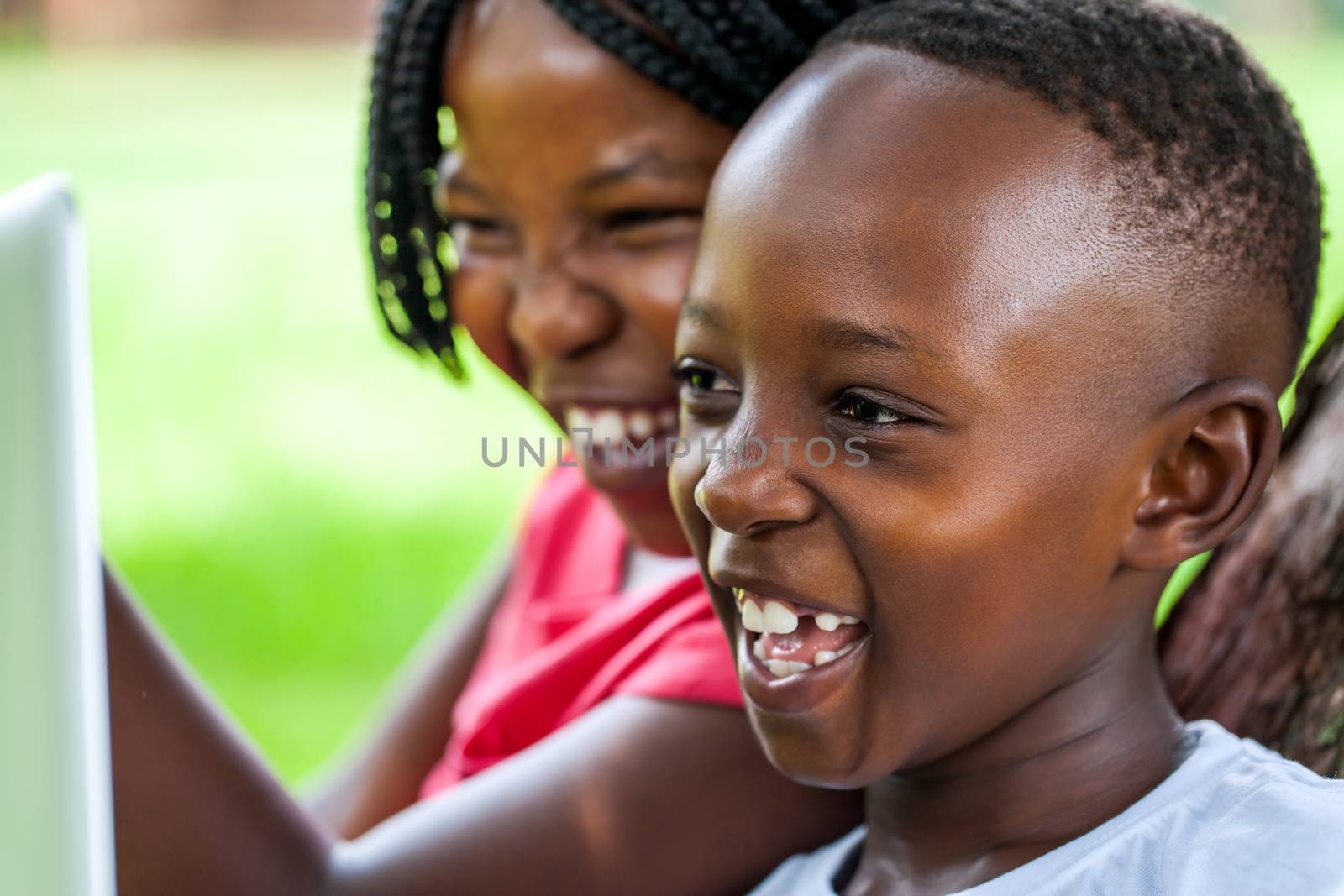 Close up face shot of African kids laughing at movie scene on digital tablet outdoors.