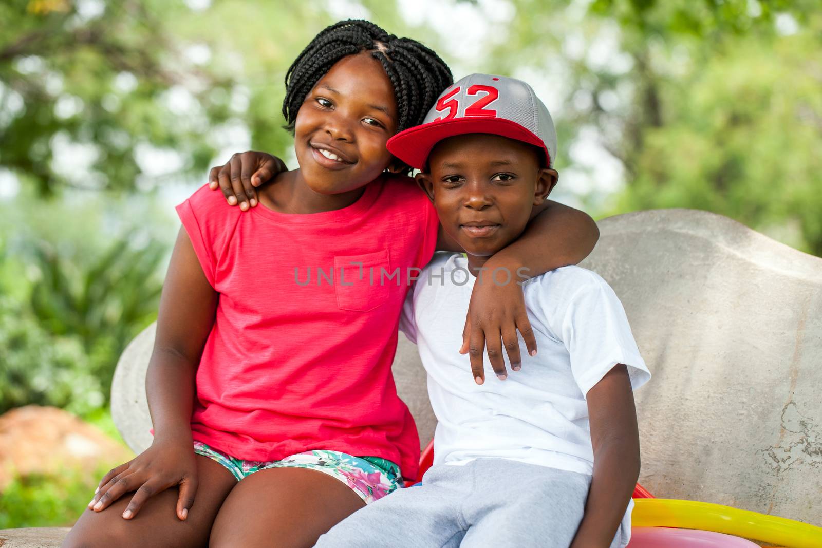 Close up portrait of two African kids sitting together on bench in park.