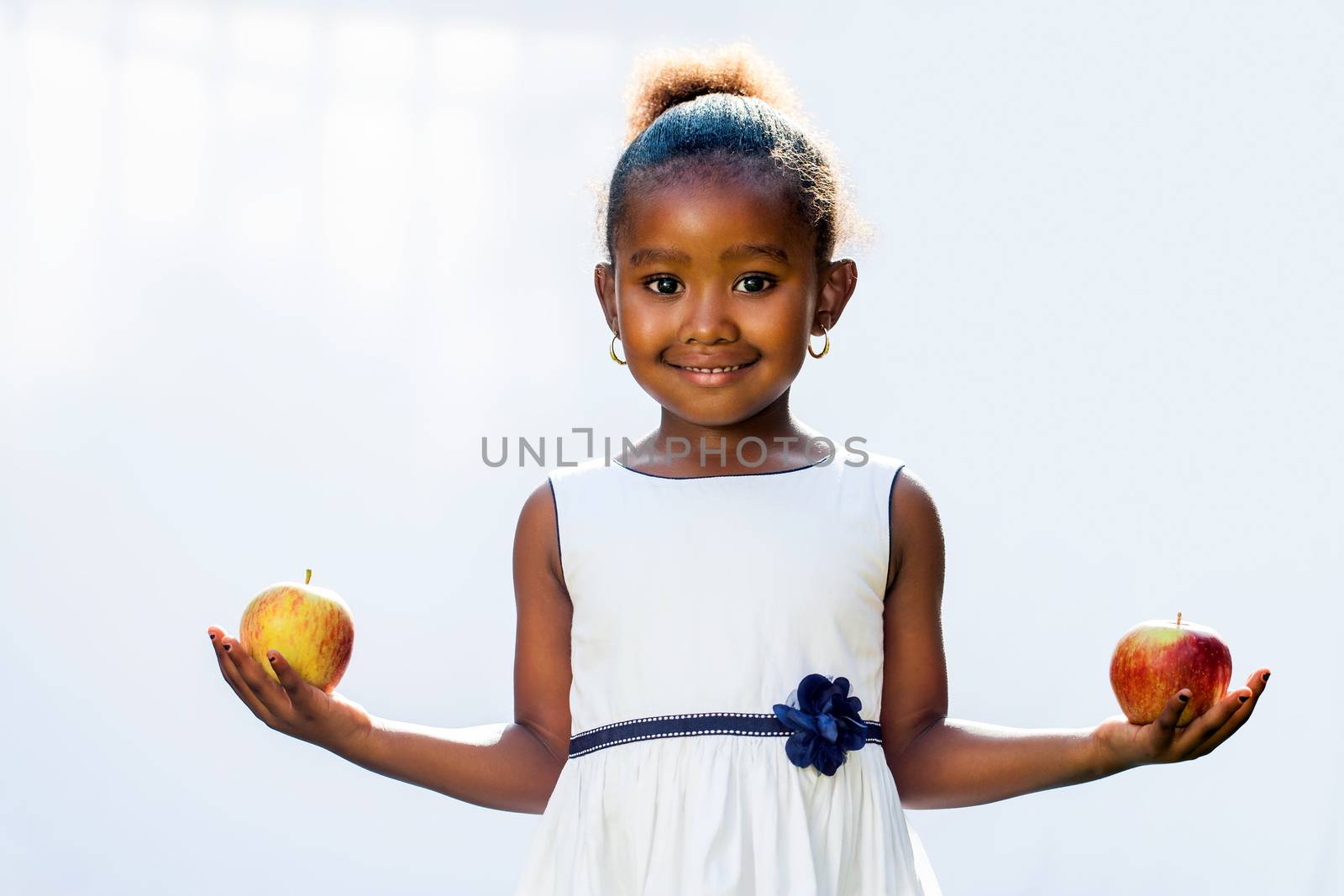 Portrait of sweet African girl holding apple in each hand.Isolated against light background.