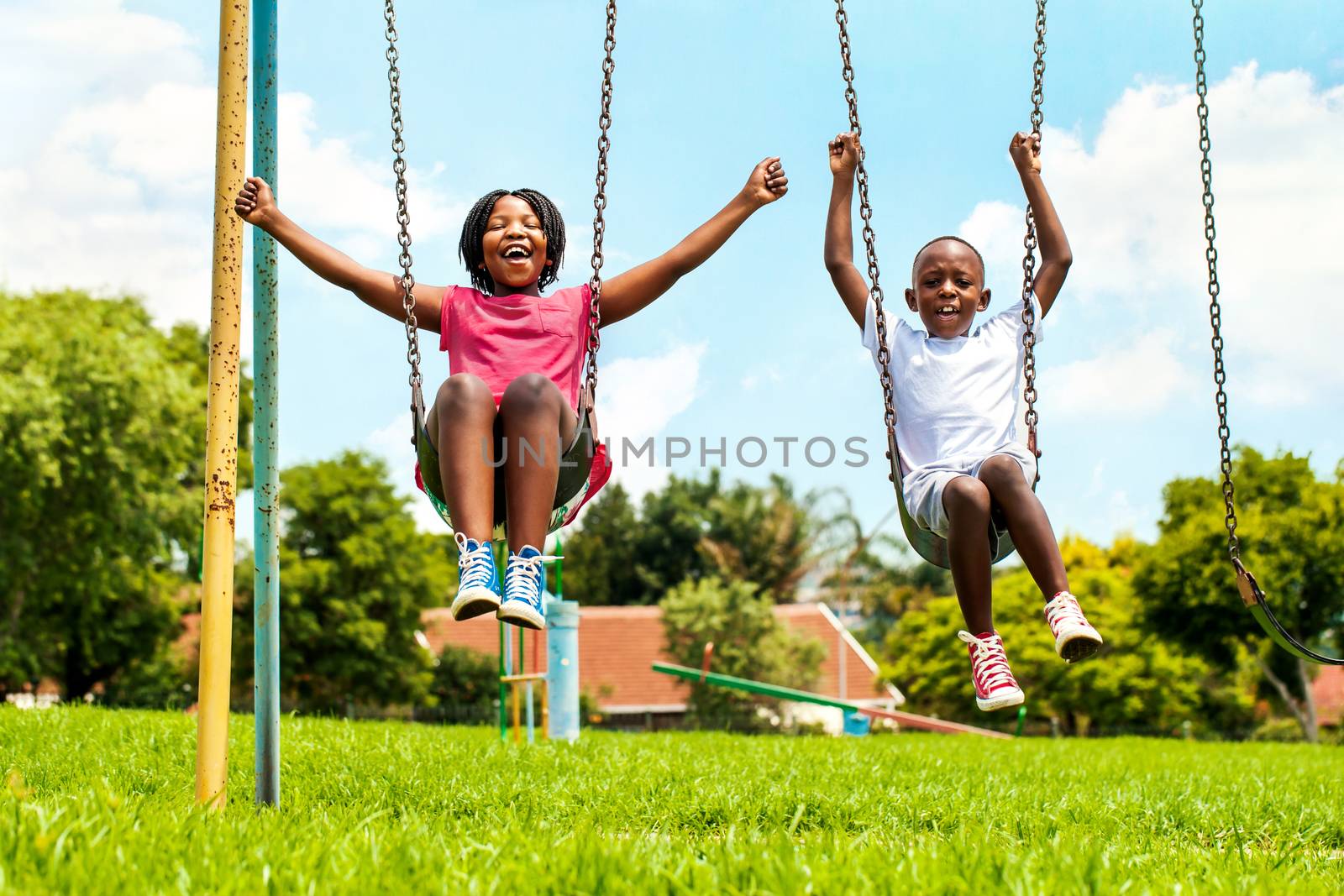 Action portrait of shouting African kids playing on swing in neighborhood.Out of focus houses in background.