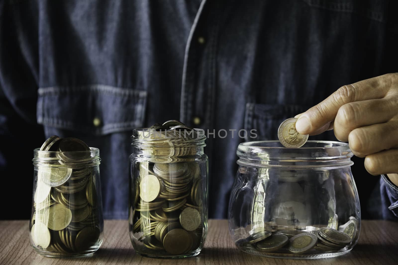 Hand putting money coin in the glass jar. Saving money, financial and accounting concept.