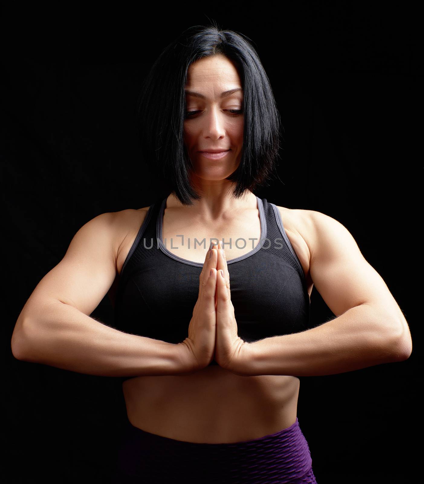 young beautiful athletic girl in a black top, hands makes a gesture of namaste with joined hands in front of the chest, black background