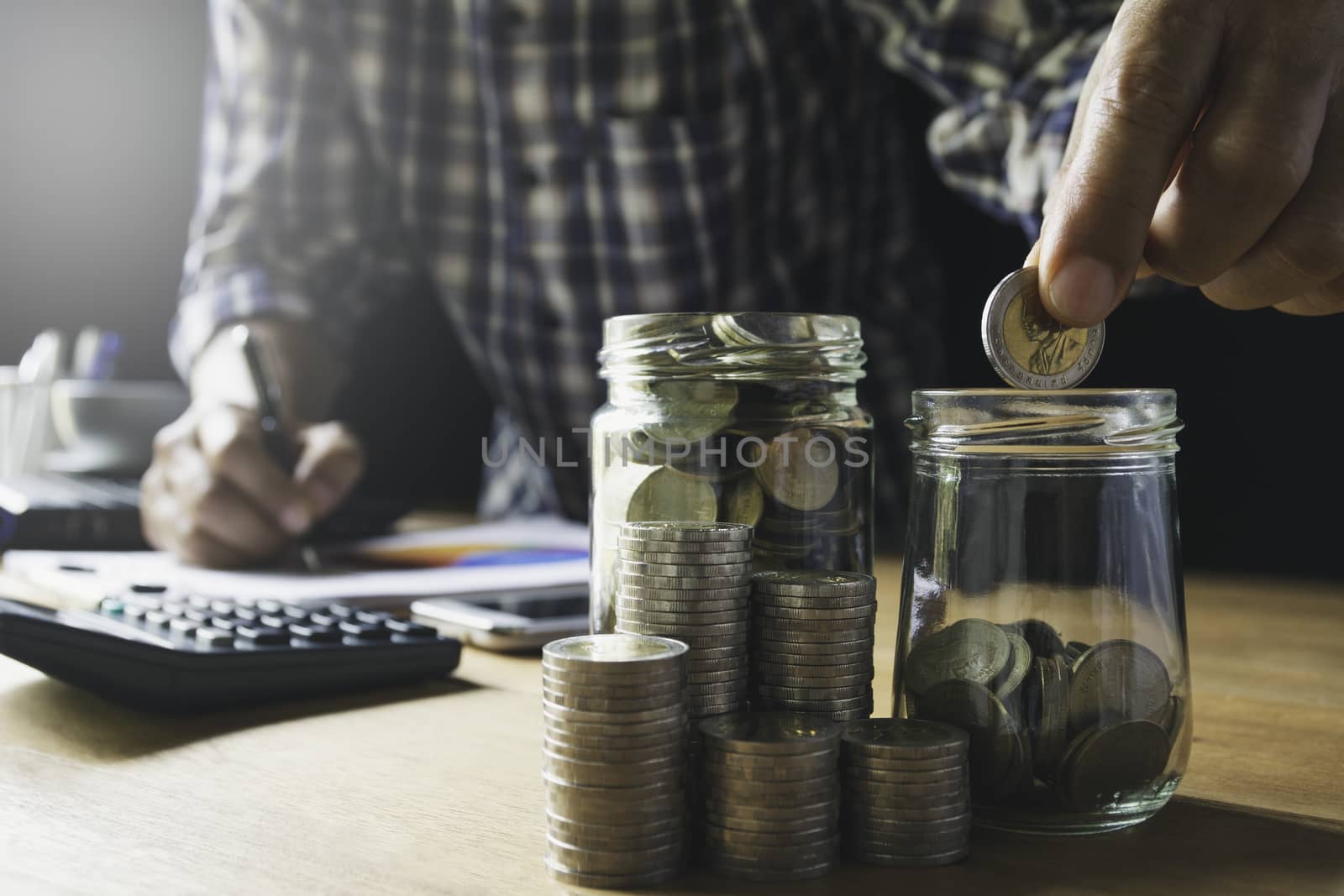 Hand putting money coin in the glass jar. Saving money, financial and accounting concept.