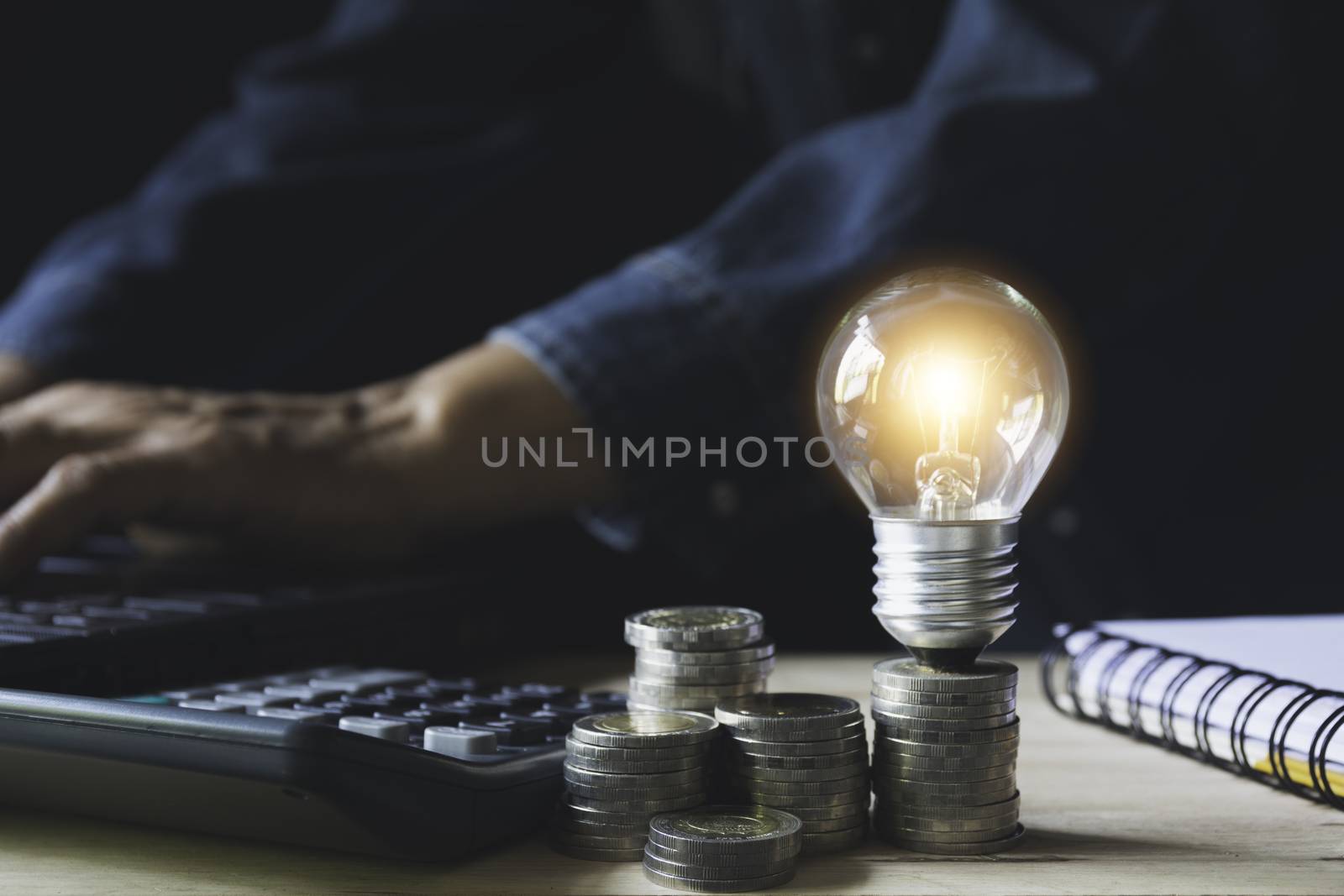 Man working with a light bulb on stack of coins for business and accounting concept.
