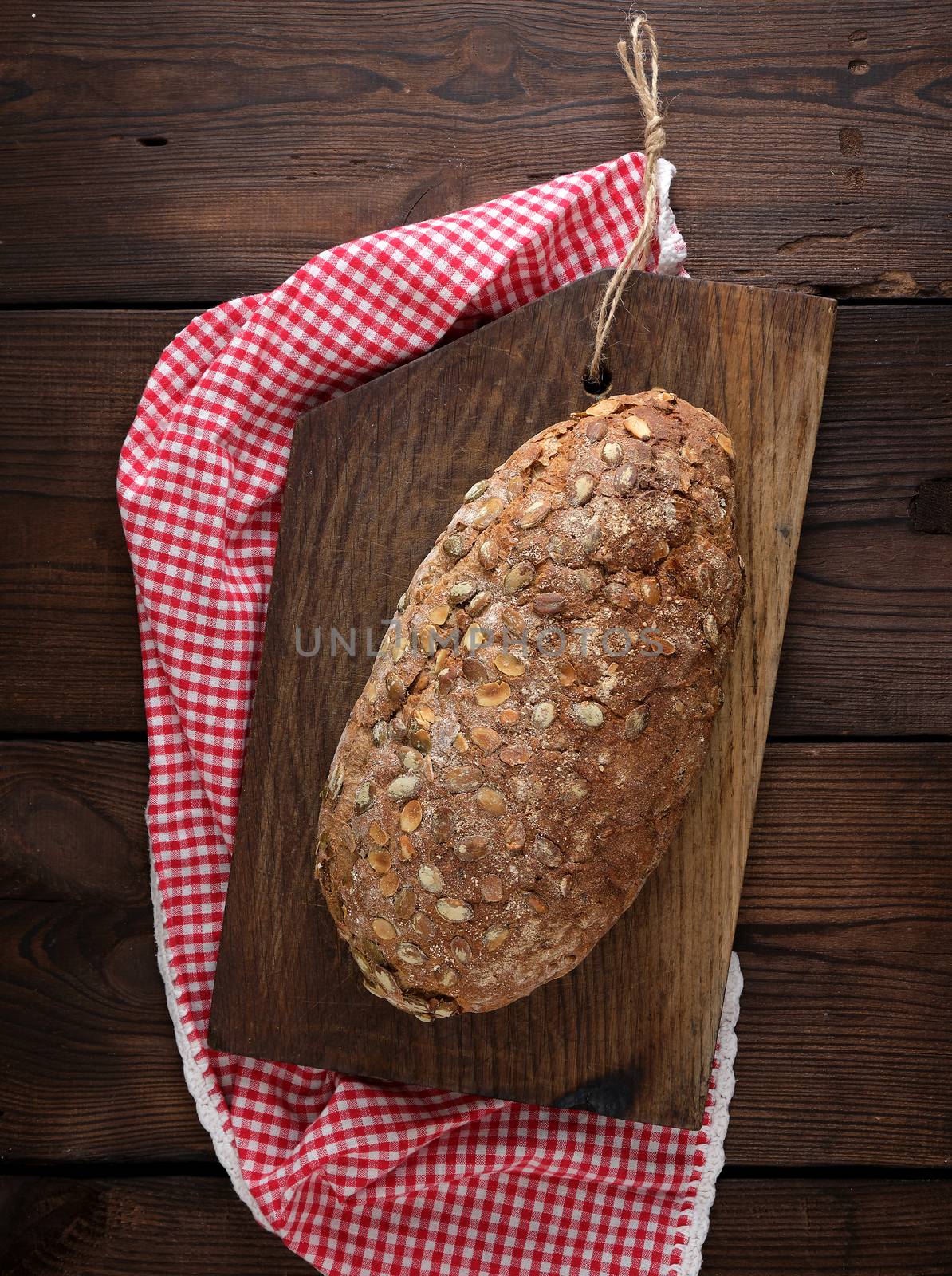 baked oval bread made from rye flour with pumpkin seeds on a red napkin, top view, copy space